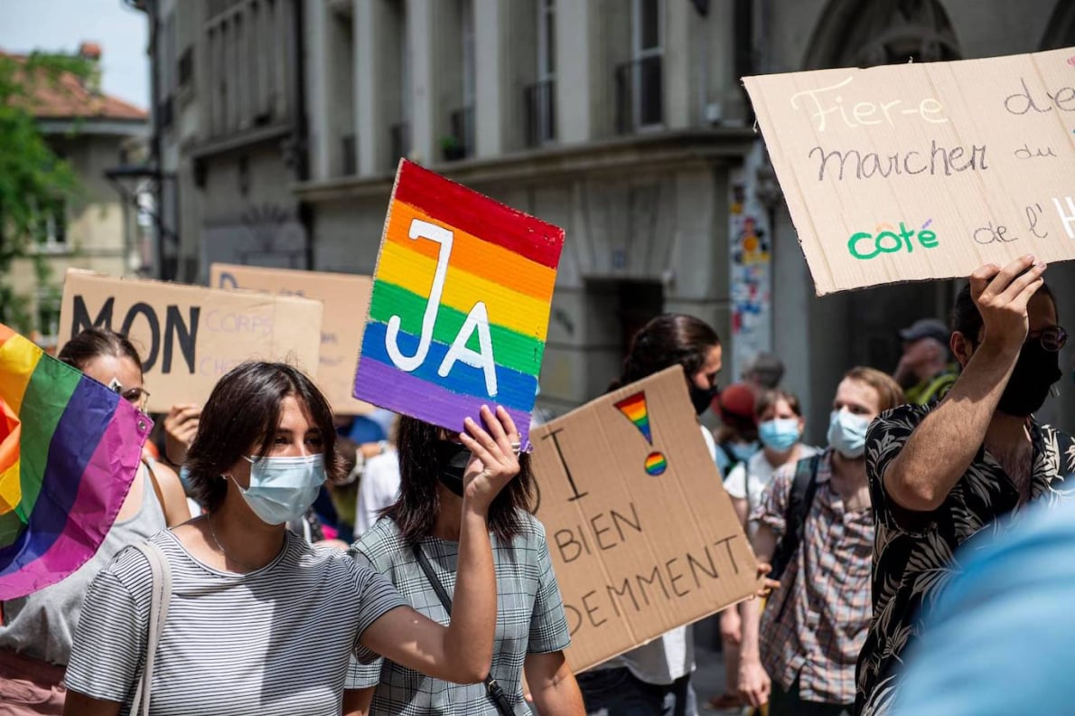 LGBTQ+ activists march in a pride demonstration holding rainbow flags and equality signs supporting human rights and inclusion.