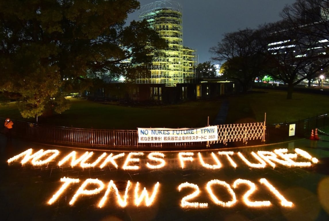 Rows of candles spell out “NO NUKES FUTURE! TPNW 2021” in front of a building at night, as part of an anti-nuclear demonstration.